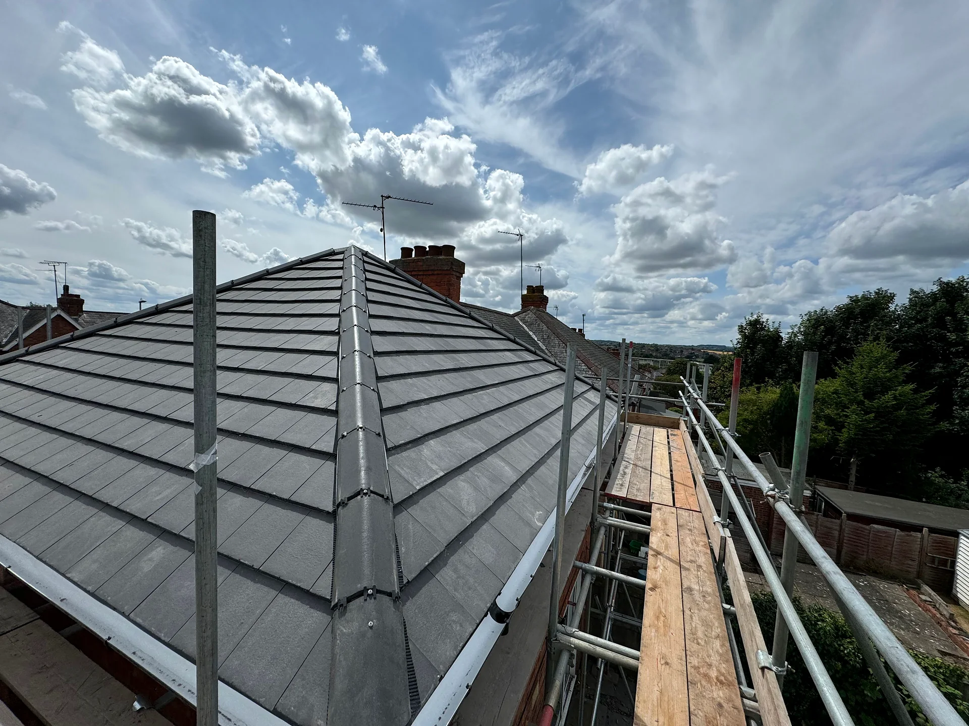 A finished hipped roof in new grey tiles, seen from the scaffold under a blue sky